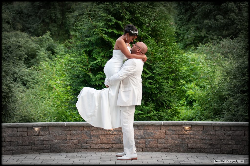 man in white holds bride up in the air in embrace